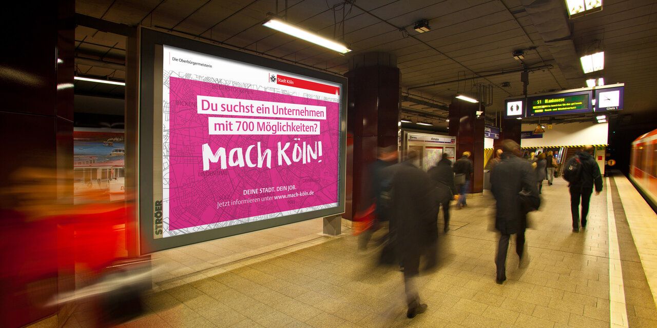 Ein Plakat mit dem Satz "Mach Köln!" an einer U-Bahn-Station.