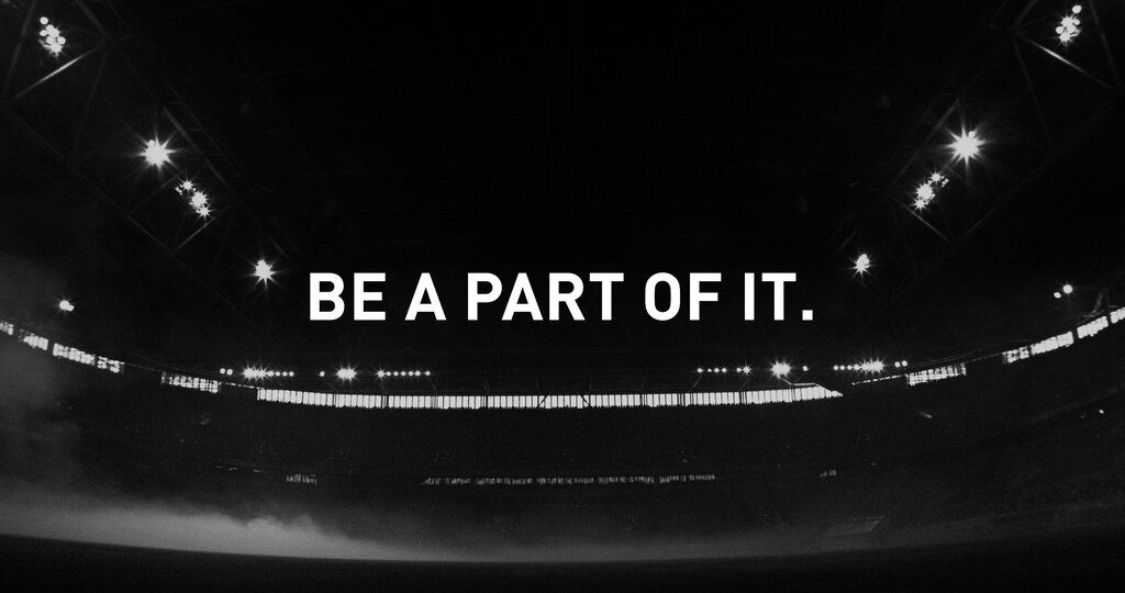 Ein Stadion im Dunkeln, darüber der Text "BE PART OF IT."