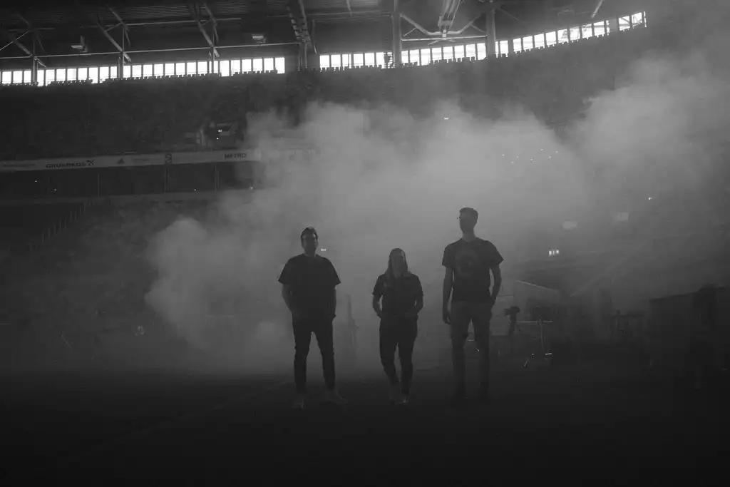 Drei Mitarbeiter der Castenow GmbH stehen im Nebel, die von einer Nebelmaschine in einer Stadionhalle produziert wird.