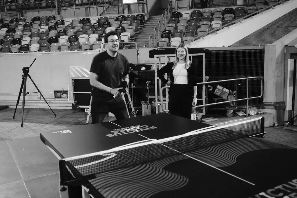 Ein Mitarbeiter der Castenow GmbH spielt Tischtennis, eine Kollegin schaut lachend zu.
