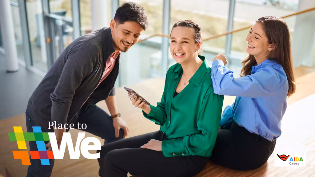 3 AIDA - Mitarbeiter sitzen gemeinsam auf einer Treppe schauen lachend auf eine Handy.