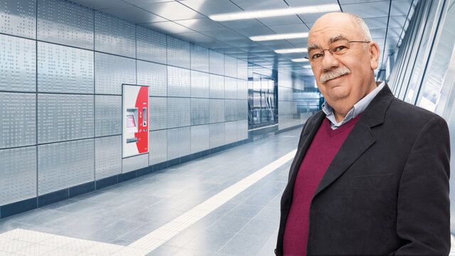 Ein älterer Mann mit Brille und Bart steht in der U-Bahn und lächelt in die Kamera