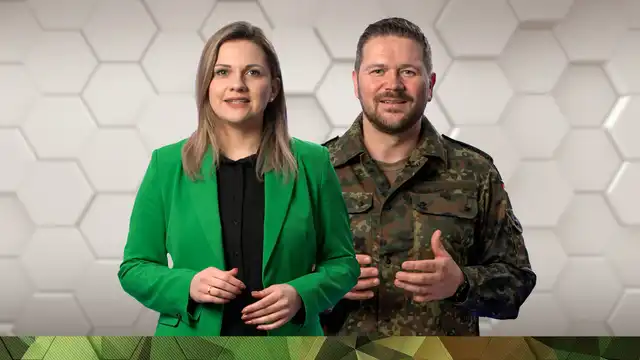 Eine Mitarbeiterin der Bundeswehr in zivil und ein Soldat in Uniform.r Werkshalle vor einem gelben Hubwagen.