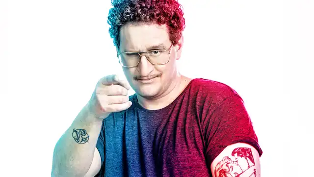 Ein Mann mit Tätowierung und Brille zeigt mit dem Zeigefinger in die Kamera.