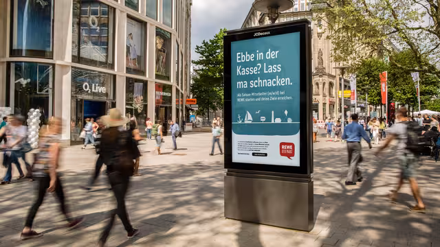 Plakat der REWE-Regionalkampagne auf einem CLP in einer belebten Innnenstadt