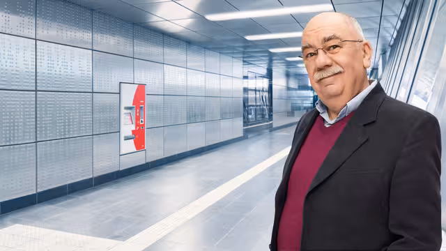 Ein älterer Mann mit Brille und Bart steht in der U-Bahn und lächelt in die Kamera