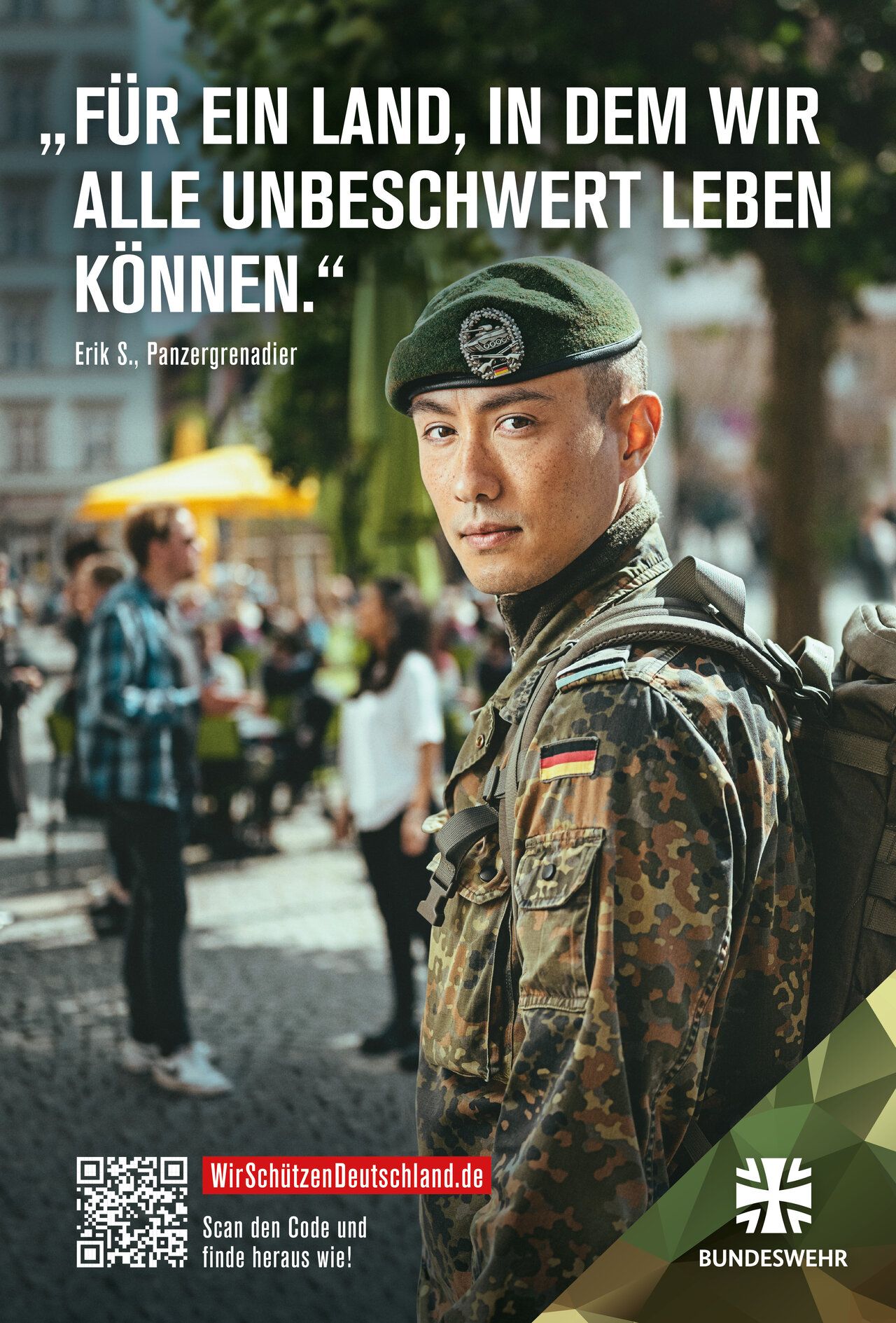 Ein Soldat in Uniform schaut über die Schulter in die Kamera, im Hintergrund sind Menschen in einer Stadt zu erkennen."Für ein Land, in dem wir alle unbeschwert leben können."