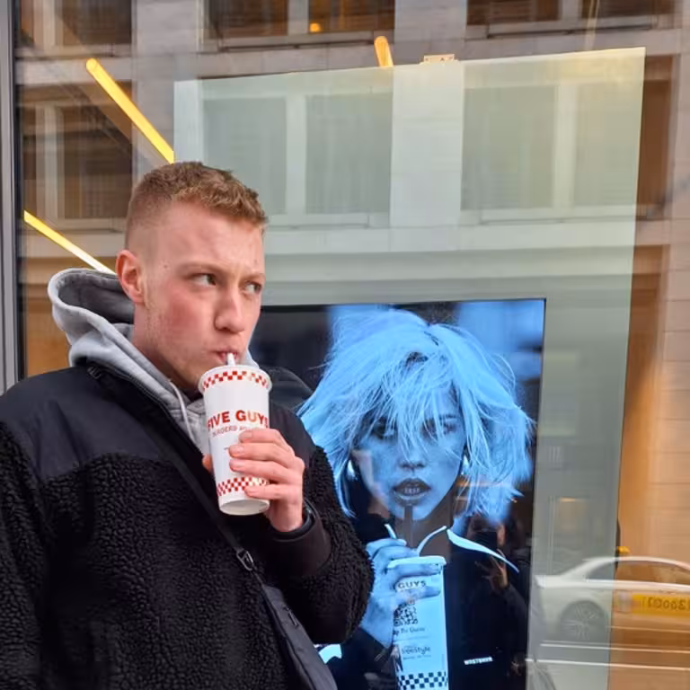 Simon Steffens, ein Mitarbeiter der Castenow GmbH, steht vor einem Schaufenster und trinkt aus einem Becher mit Strohhalm.