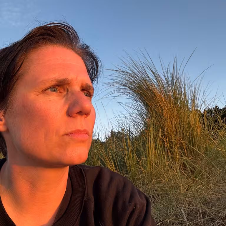 Martit Gottschlich, Mitarbeiterin der Castenow GmbH, sitzt am Meer, die untergehende Sonne erhellt ihr Gesicht.