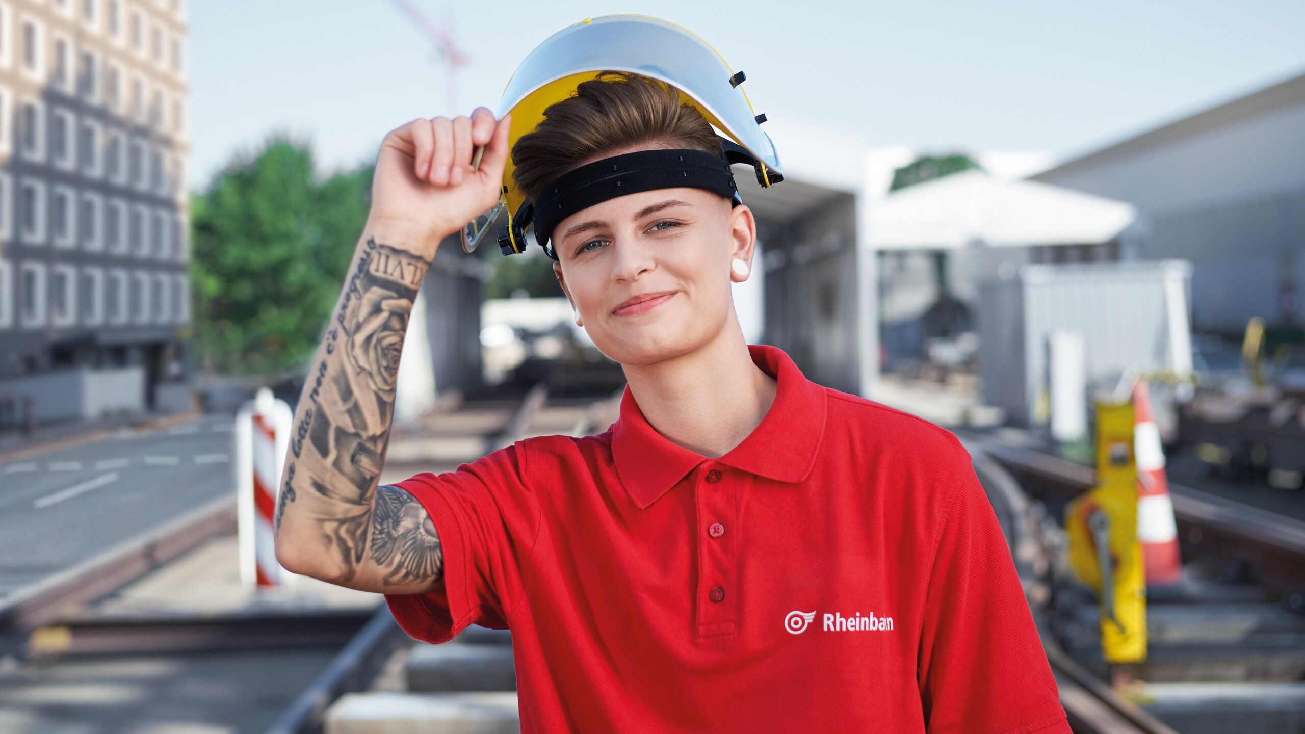 Eine junge Mitarbeiterin der Rheinbahn lacht mit Helm auf dem Kopf in die Kamera.