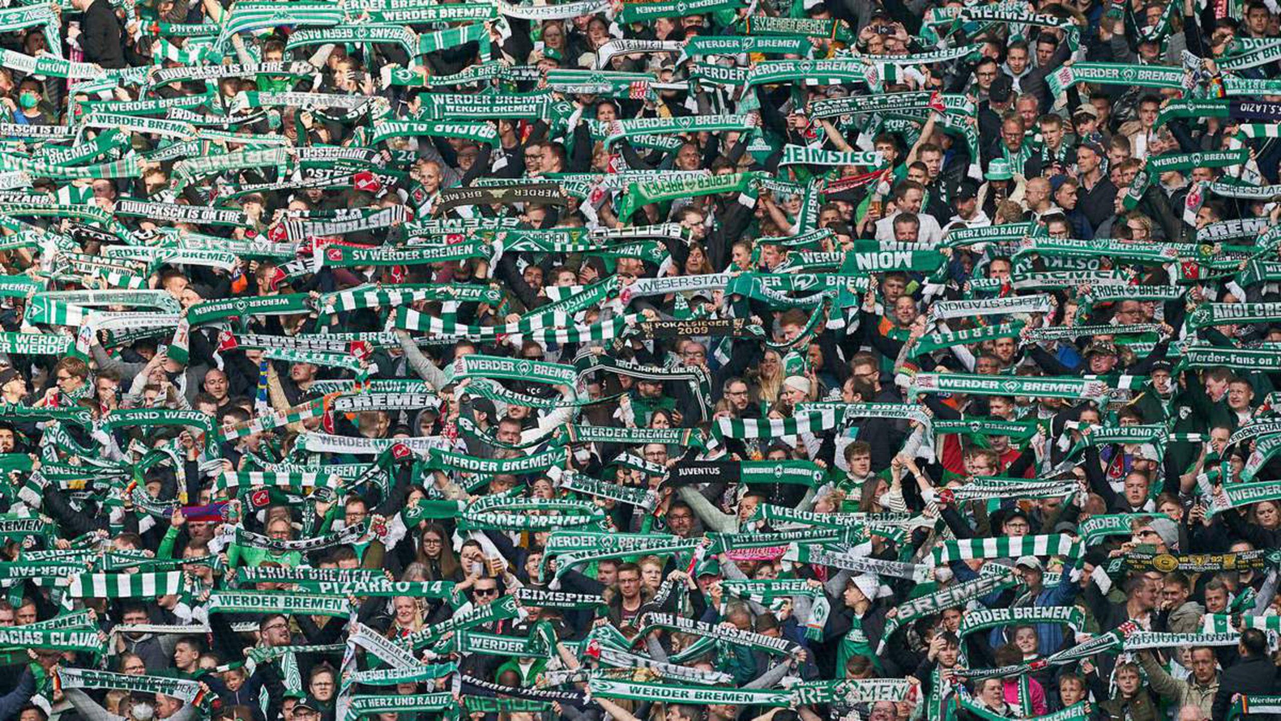 Eine Masse an Fußballfans des Vereins Werder Bremen, die ihren grünen Schal hochhalten.