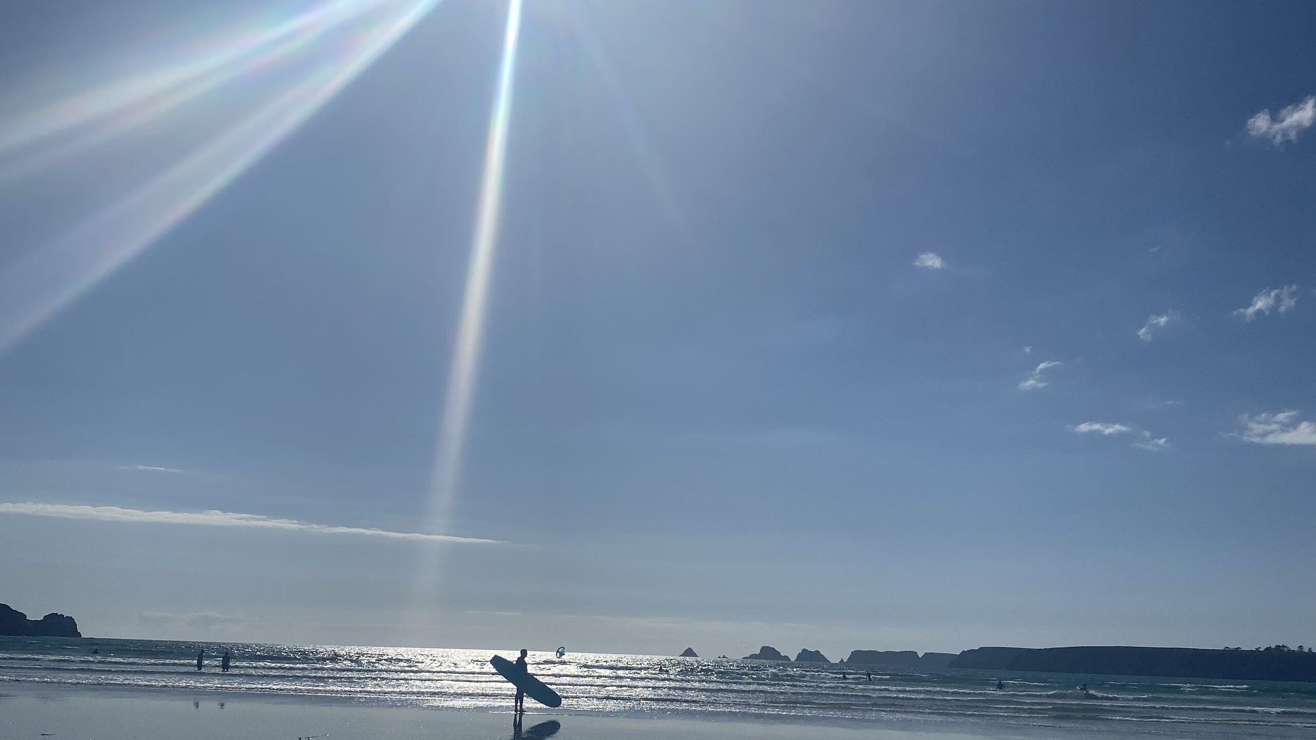 Am Strand. Blauer Himmel, Sonnenschein und ein einsamer Surfer mit seinem Board unter dem Arm.