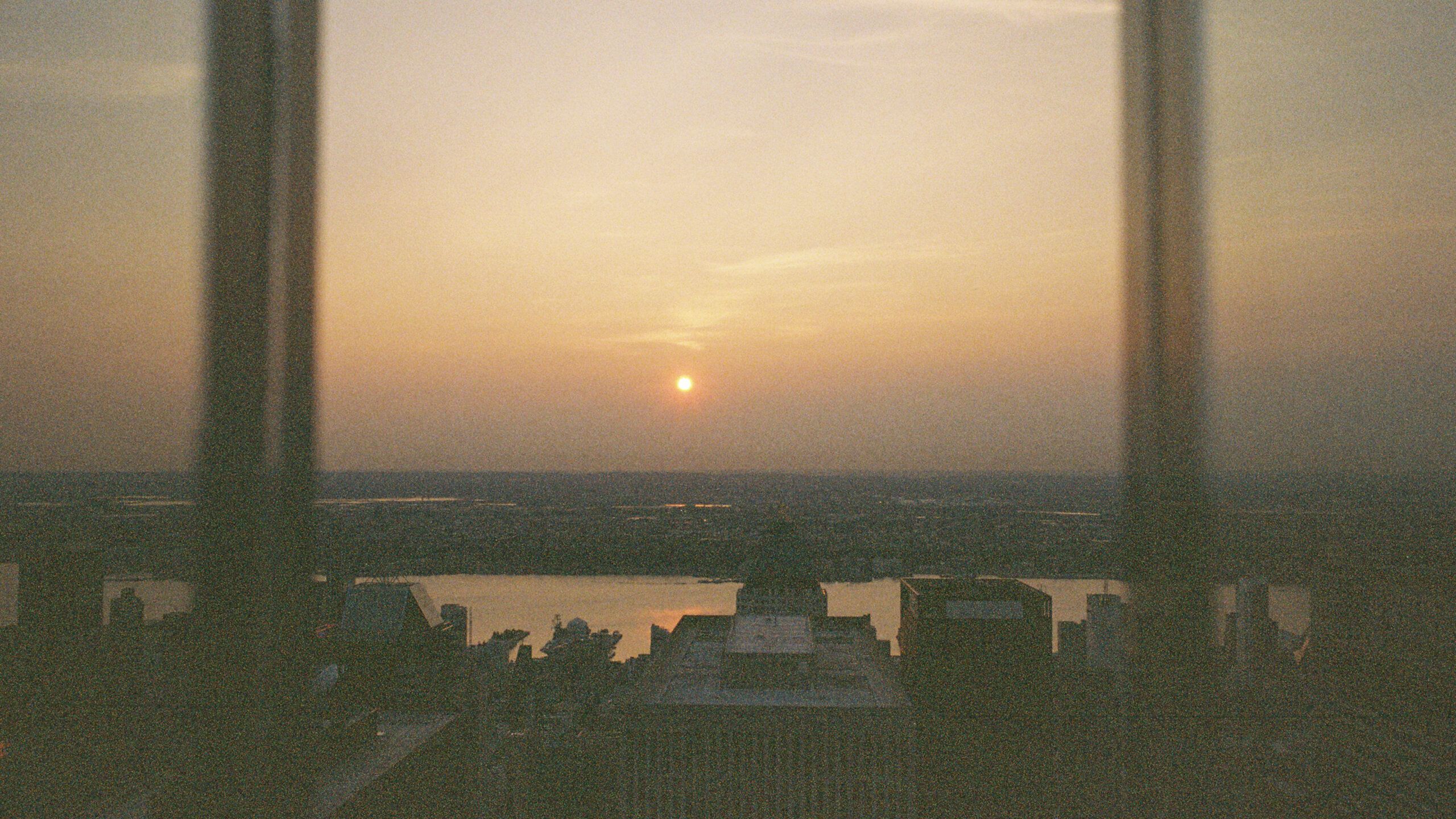 Ein Sonnenuntergang über einer Stadt, aus einem Hochhausfenster fotografiert.
