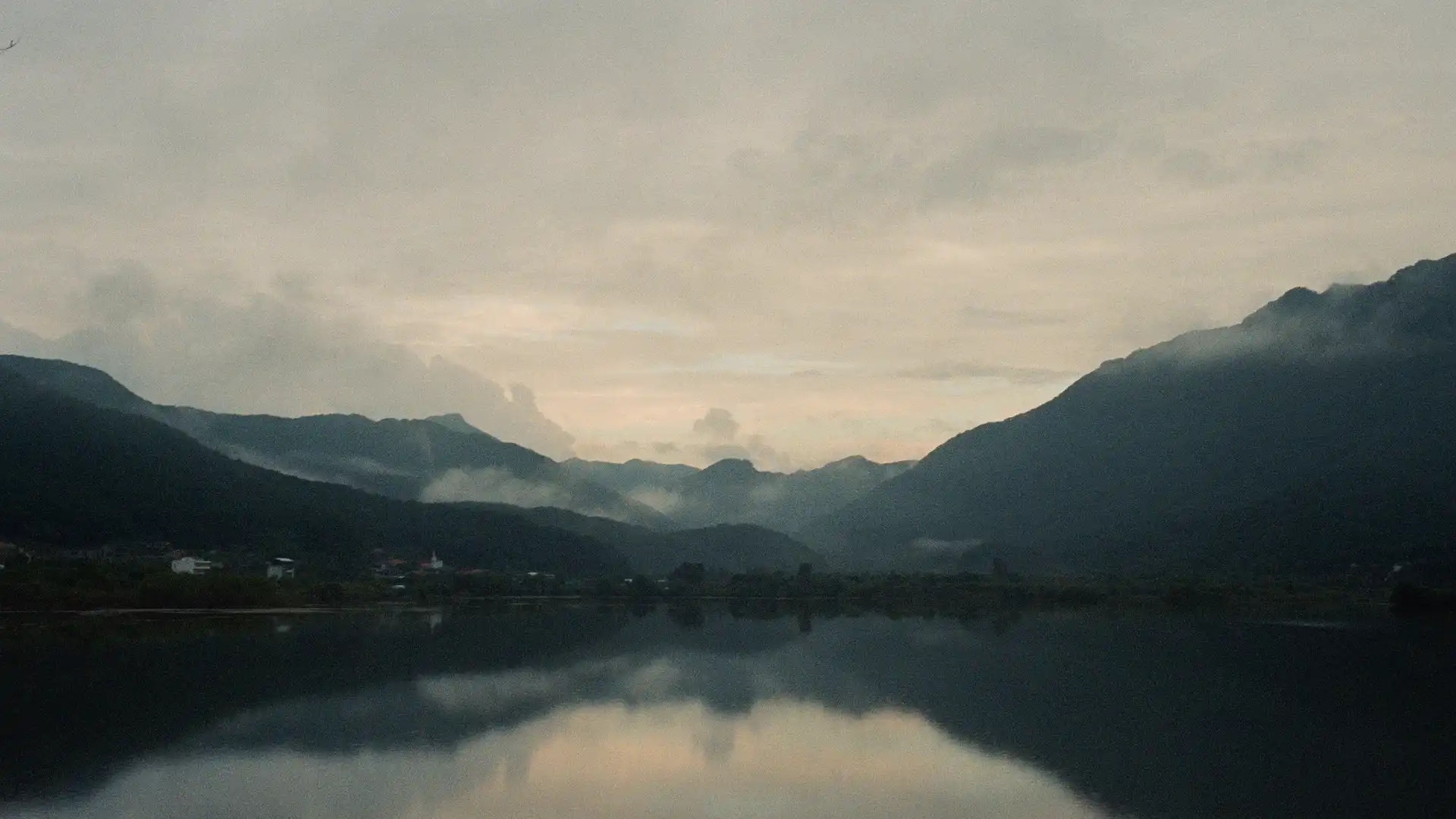 Der Blick über einen See auf Berge, die unter Wolken liegen.