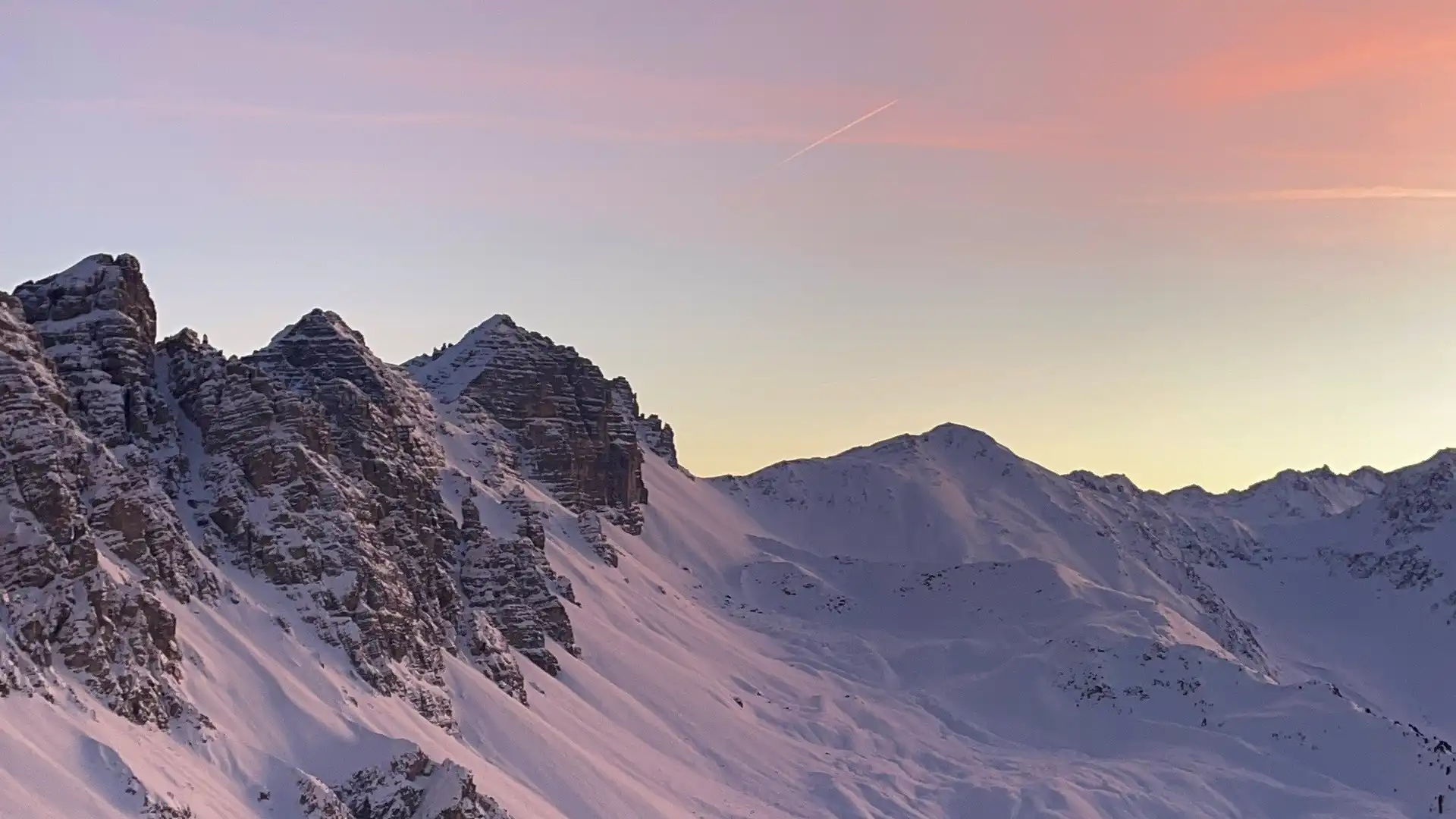 Ein Sonnenuntergang hinter schneebedeckten Bergen.