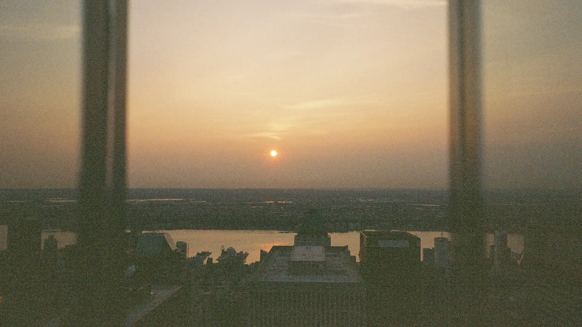 Ein Sonnenuntergang über einer Stadt, aus einem Hochhausfenster fotografiert.