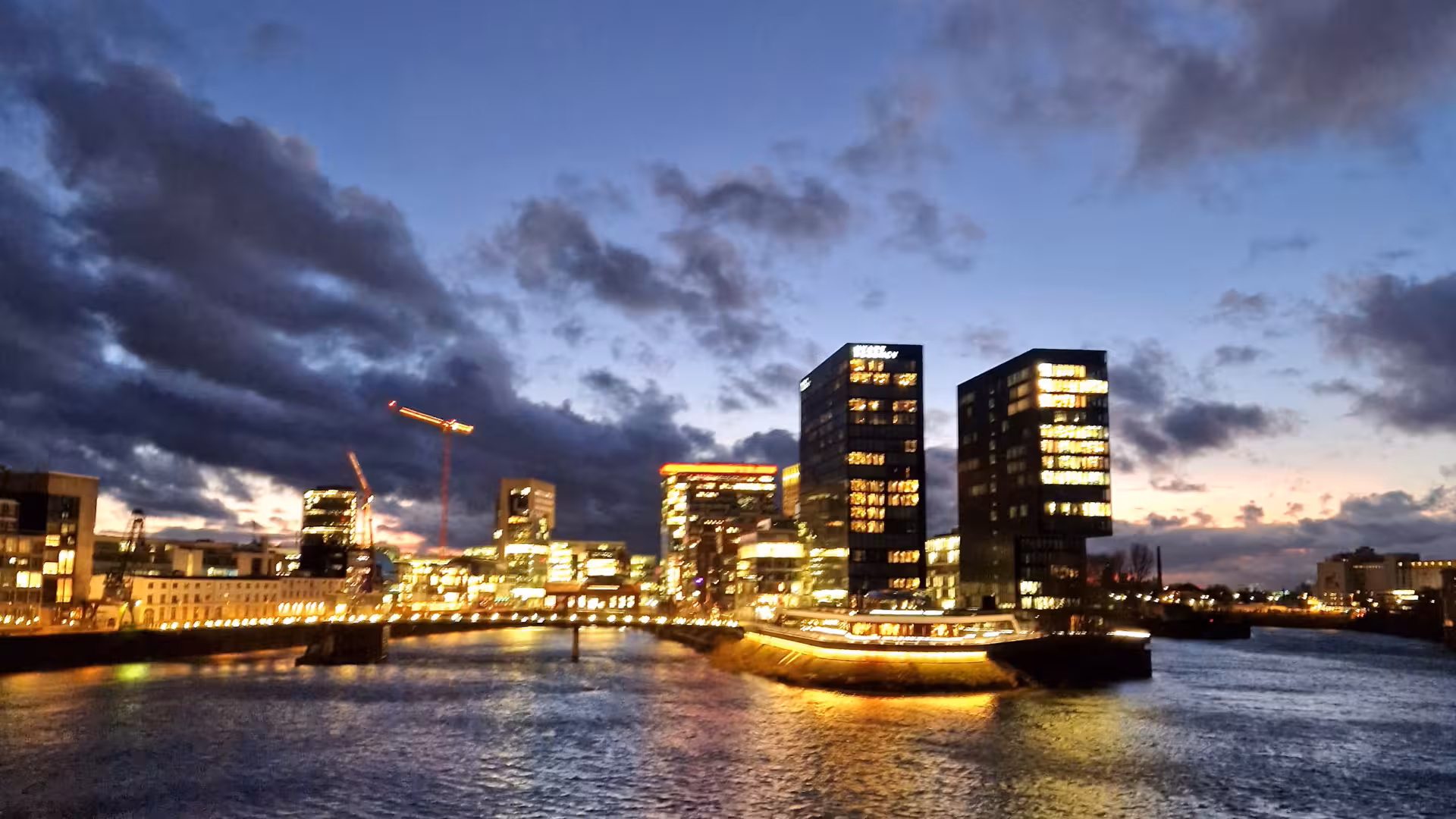 Beleuchtete Hochhäuser in Düsseldorf, die vom Rhein aus während der Dämmerung fotografiert wurden.