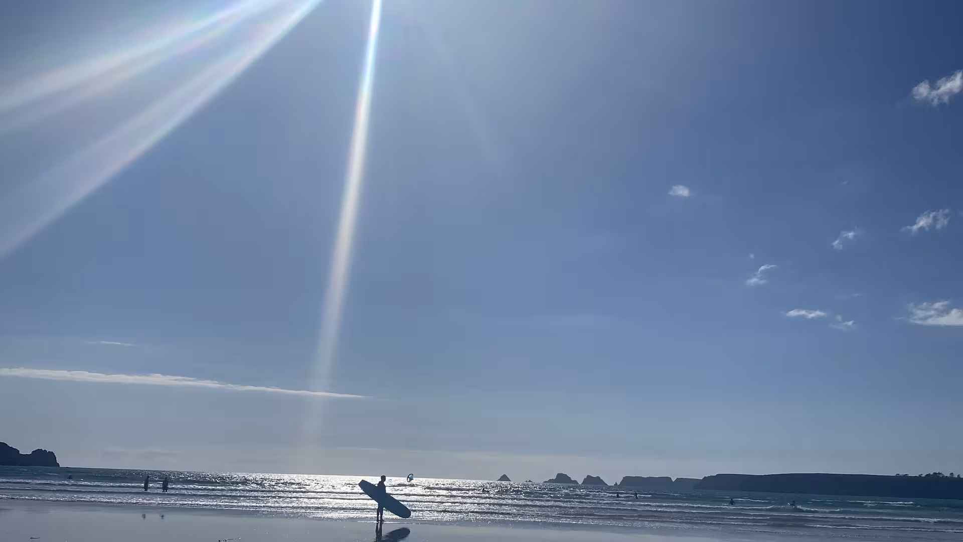 Am Strand. Blauer Himmel, Sonnenschein und ein einsamer Surfer mit seinem Board unter dem Arm.