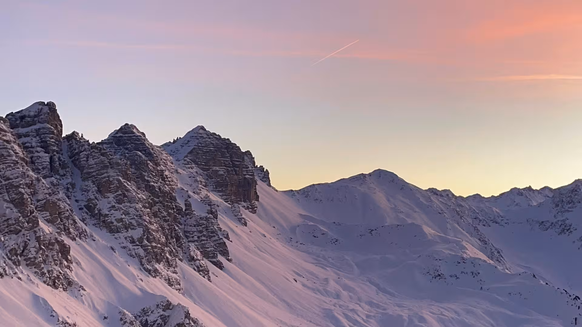 Ein Sonnenuntergang hinter schneebedeckten Bergen.