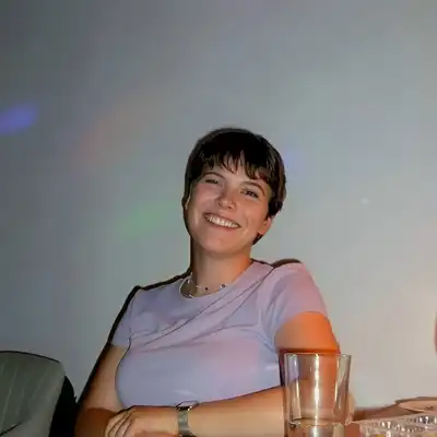 Justine Schelp, Mitarbeiterin der Employer Branding Agentur Castenow, sitz mit einem Glas Wasser an eine Tisch und lacht in die Kamera.