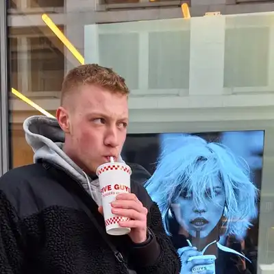 Simon Steffens, ein Mitarbeiter der Castenow GmbH, steht vor einem Schaufenster und trinkt aus einem Becher mit Strohhalm.