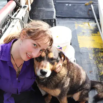 Louisa Cayenne Moreth, Mitarbeiterin der Castenow GmbH, sitzt auf einem Boot und umarmt einen Hund.
