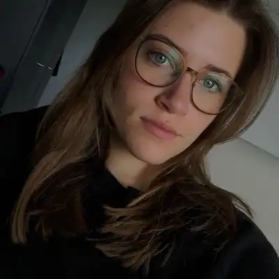 Talia Hinz, Mitarbeiterin der Castenow GmbH, trägt einen schwarzen Pullover, eine Brille und lange dunkelblonde Haare.