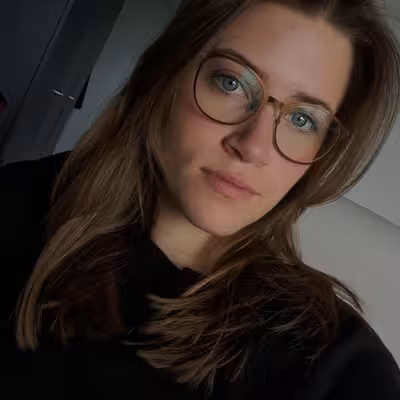 Talia Hinz, Mitarbeiterin der Castenow GmbH, trägt einen schwarzen Pullover, eine Brille und lange dunkelblonde Haare.