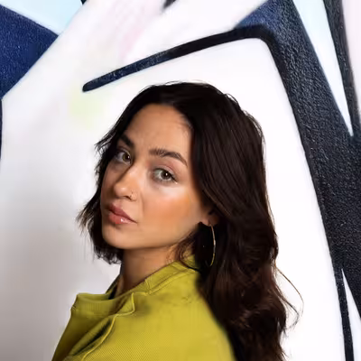 Ceyda Dogan, Mitarbeiterin der Castenow Gmbh, steht vor eine Graffitiwand und schaut über die Schulter in die Kamera.