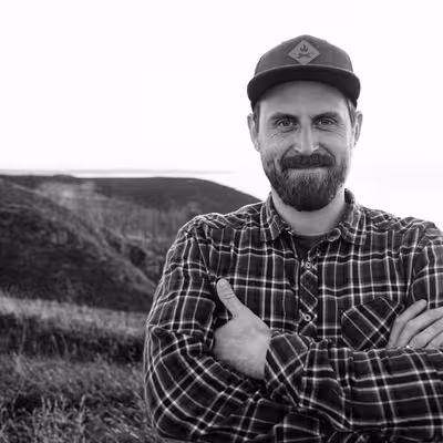 David Rösler, Mitarbeiter der Castenow GmbH, steht mit verschränkten Armen an der Meeresküste und lacht in die Kamera.